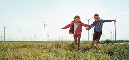 Due bambini giocano in un campo con turbine eoliche sullo sfondo