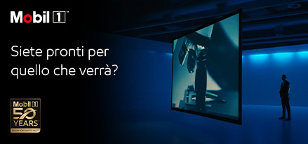 Un uomo in piedi davanti a un grande schermo, che guarda un film, con il logo dei 50 anni di Mobil 1 e un testo che dice: Are you ready for what;s next?